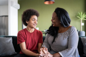 Mother and son together holding hands sitting on the couch at home, LGBTQIA