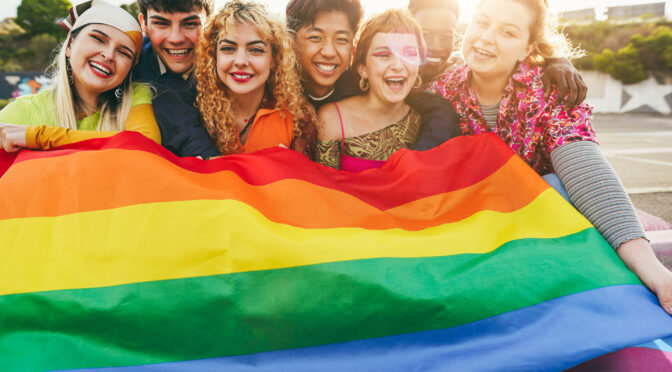 Young diverse people having fun holding LGBT rainbow flag outdoor