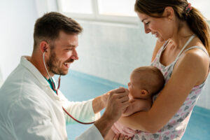 Happy pediatrician doctor with baby checking possible heart defect. Healthcare, people concept