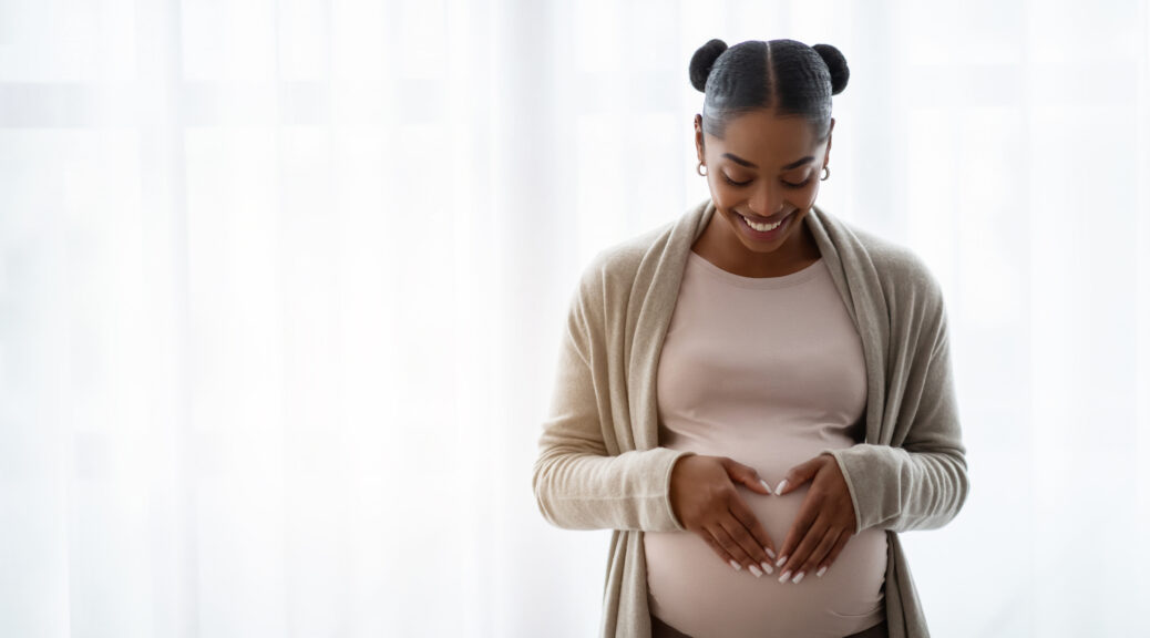 Smiling pregnant woman wearing comfy clothing holding hands on her big belly, enjoying her pregnancy, expecting baby, standing by window at home, panorama with copy space