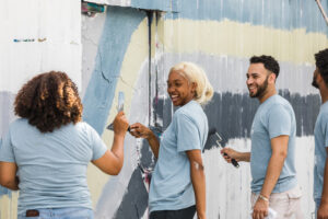 The group of young adult use their painting supplies to work on the art mural they are completing.