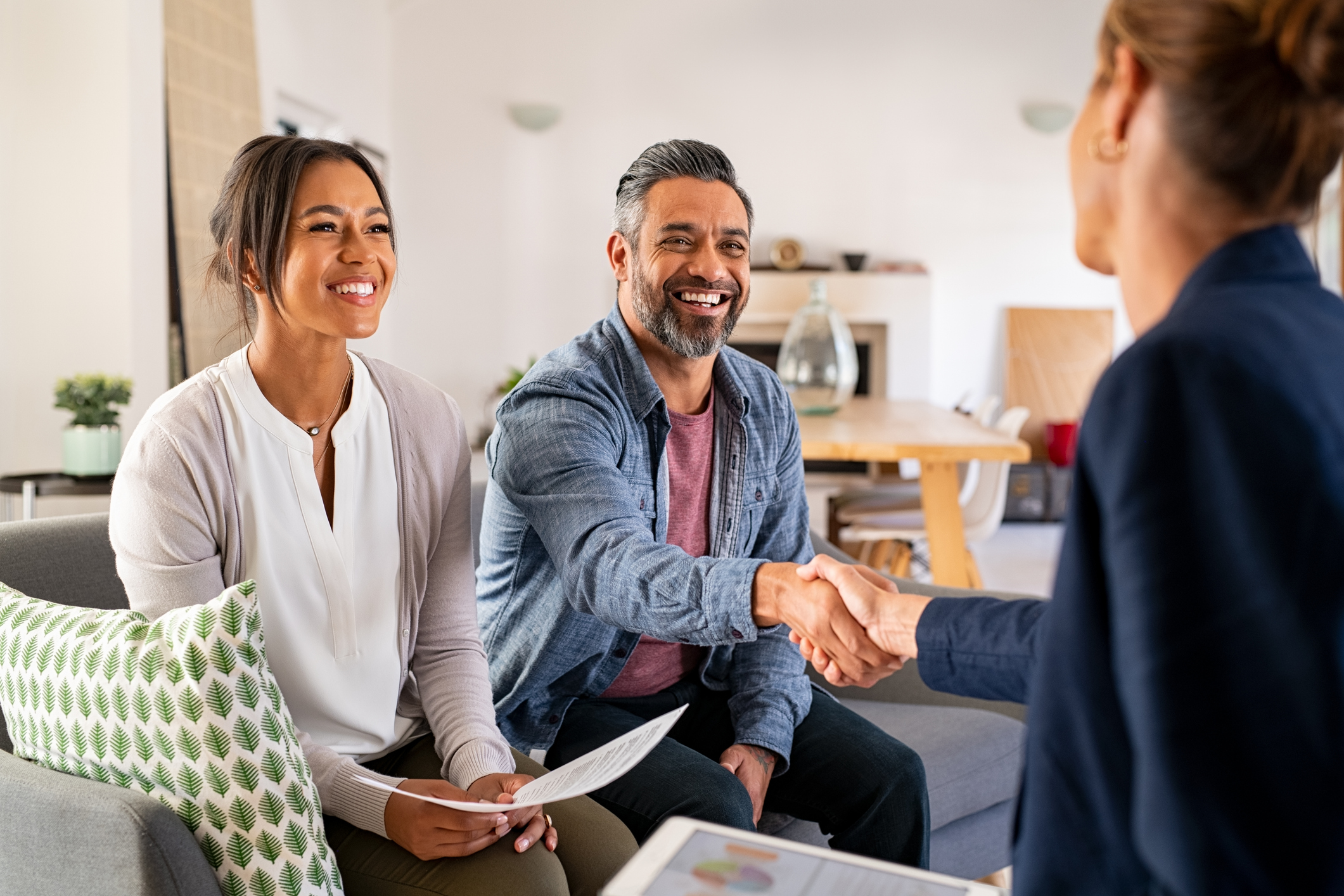 Happy smiling couple greeting broker with handshake at home.